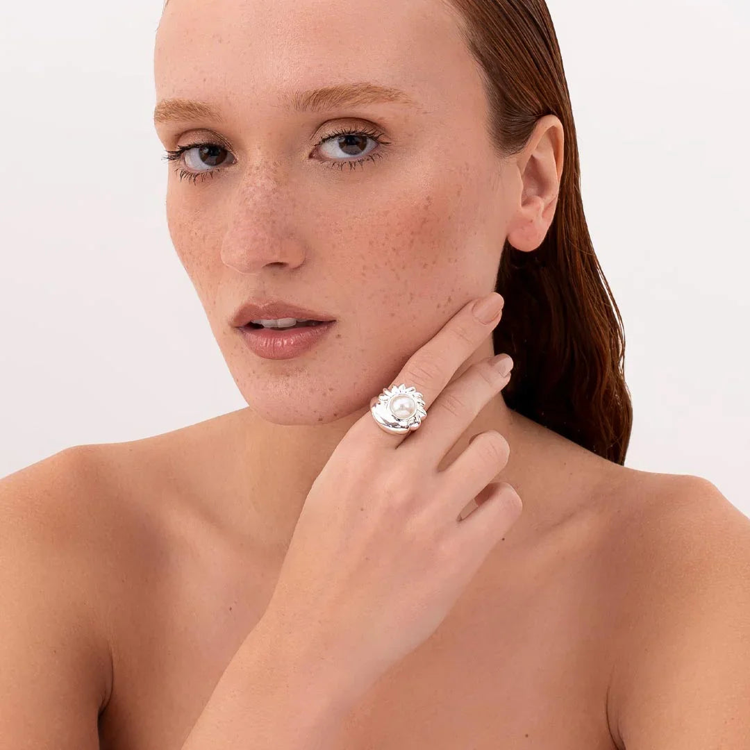 Woman wearing a contemporary silver ring with a large pearl, close-up on hand and face.