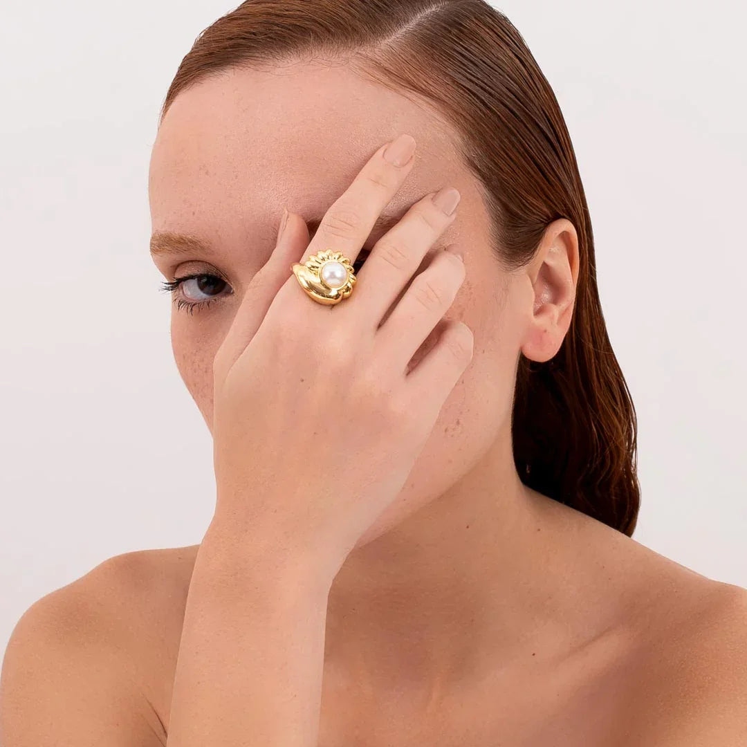 Woman wearing a gold statement ring with pearl detail, contemporary jewelry style