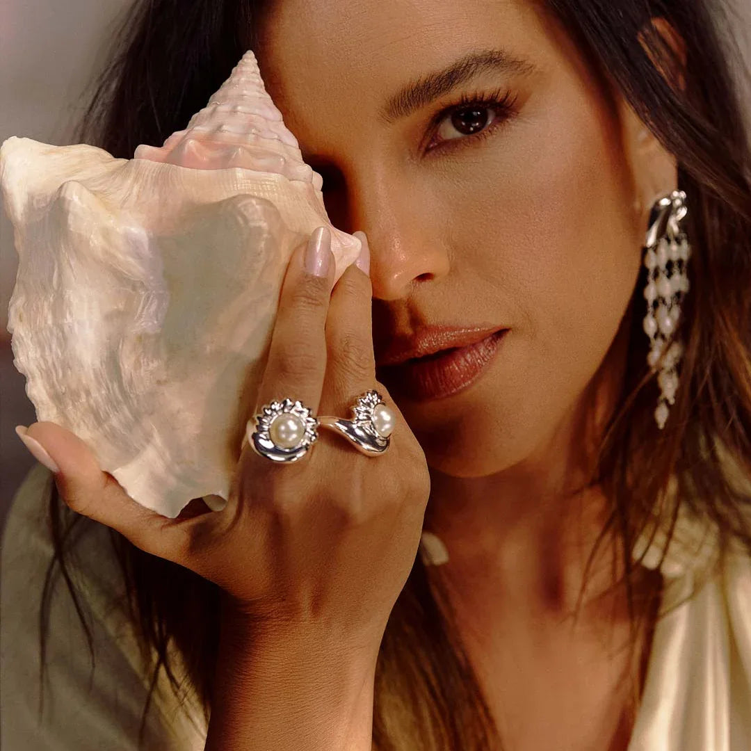Woman holding seashell, wearing pearl statement ring and silver jewelry, elegant setting