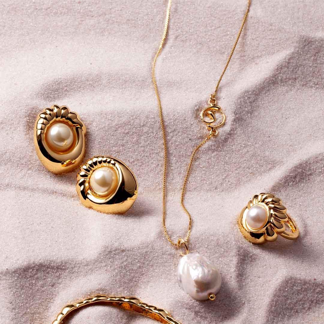 Gold jewelry set with pearls, including earrings, ring, bracelet, and necklace on sand