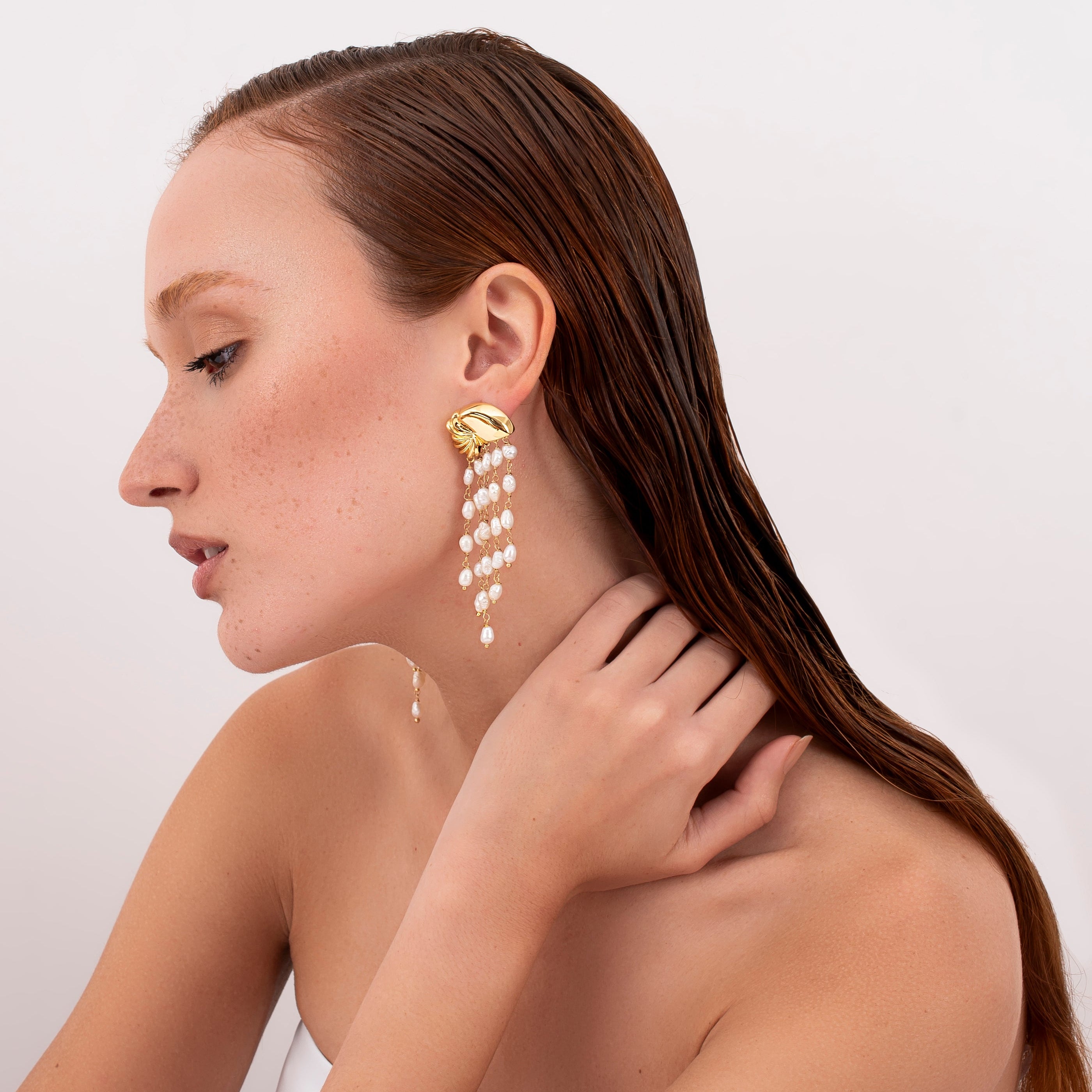 Model wearing statement pearl cascade earrings with sculptural gold design