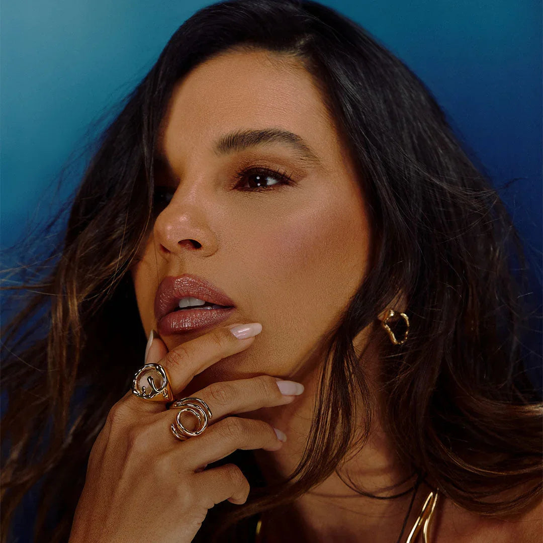 Woman wearing gold statement rings and gold hoop earring against blue background